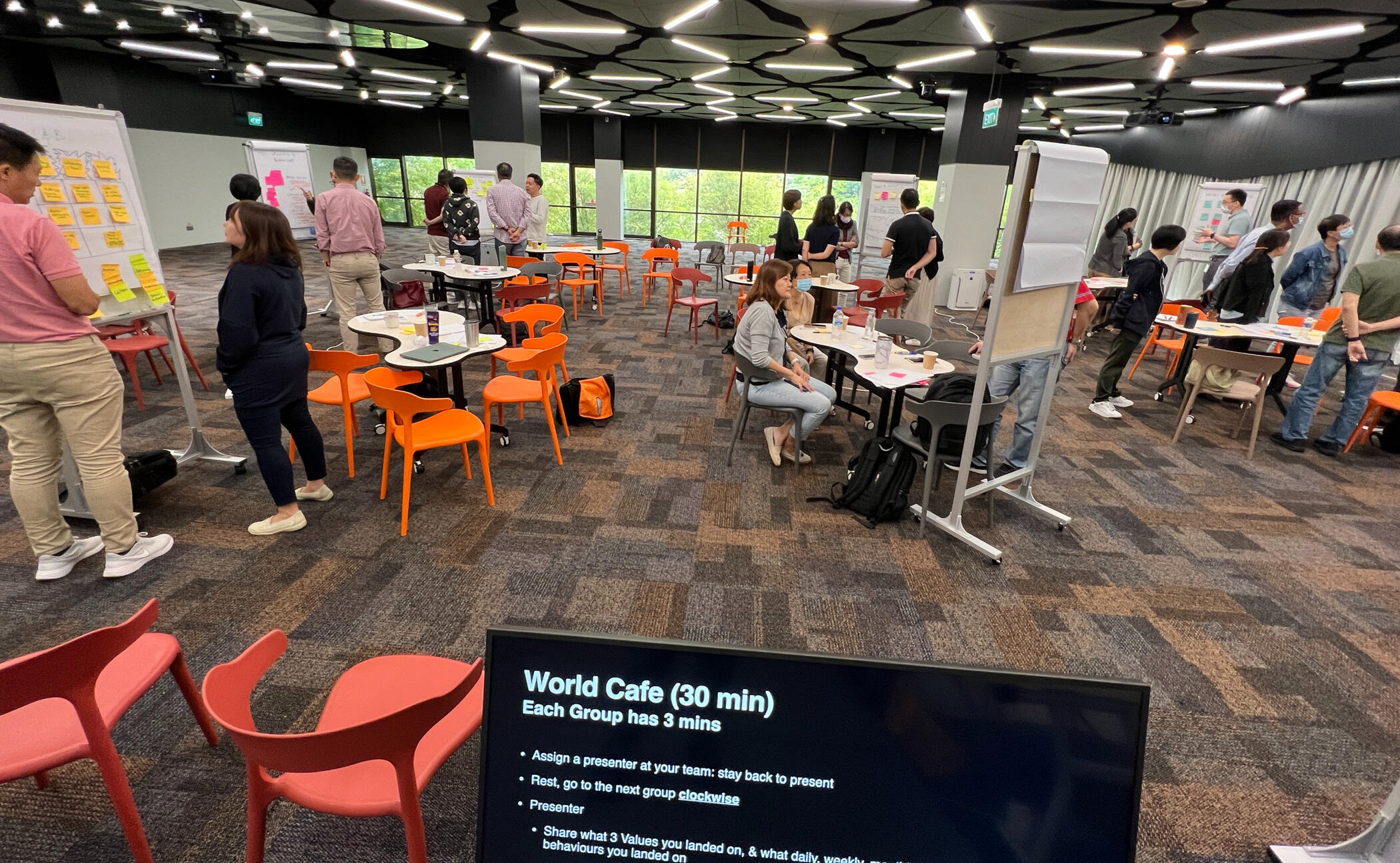 Computer screen edge in a meeting room, with people writing in the background