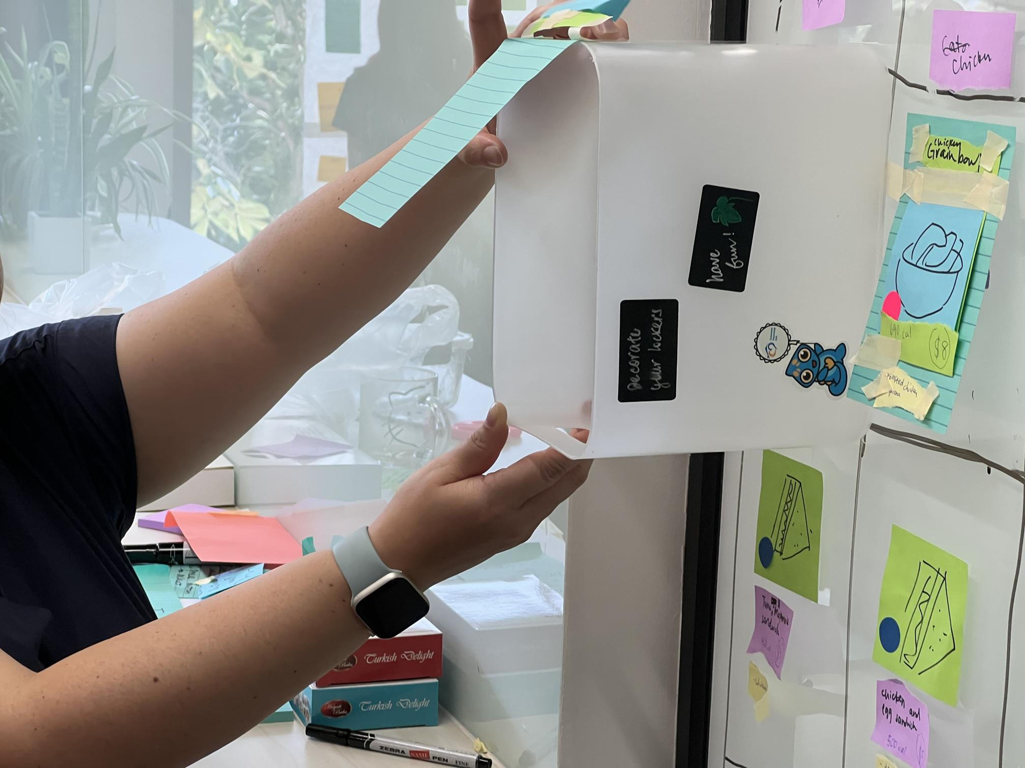 A lady touching a Post It on a phone, while another person records a video & another interviews.